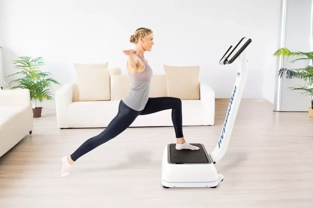 Top Vibration Plate Exercises: A Complete Guide To Safe Whole-Body Vibration Workouts 9 Woman in a living room setting performing a forward lunge with her lead foot on a vibration plate.