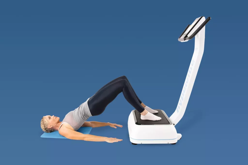 Top Vibration Plate Exercises: A Complete Guide To Safe Whole-Body Vibration Workouts 10 A woman performing a glute bridge with her feet on a vibration plate and her shoulders on a blue yoga mat.