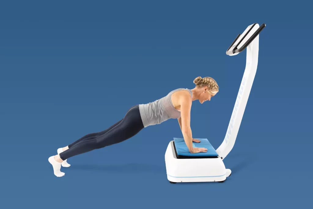 Top Vibration Plate Exercises: A Complete Guide To Safe Whole-Body Vibration Workouts 14 Woman in a high plank position with hands placed on a blue cushion on a vibration plate.