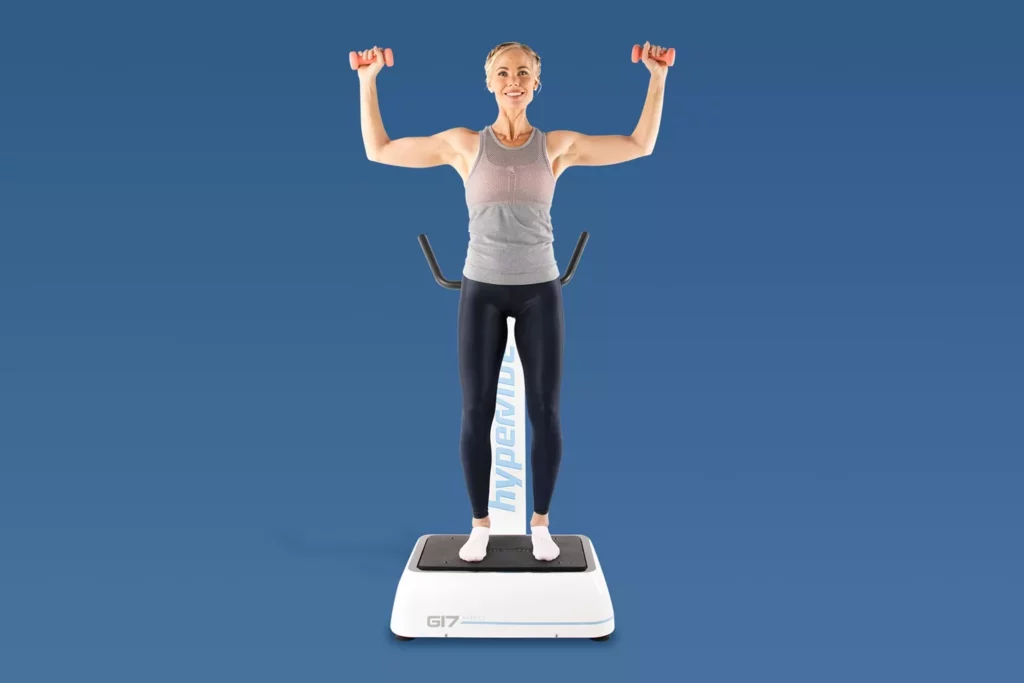 Top Vibration Plate Exercises: A Complete Guide To Safe Whole-Body Vibration Workouts 13 A woman performing an overhead shoulder press with light dumbbells while standing on a Hypervibe G17 Pro vibration plate.