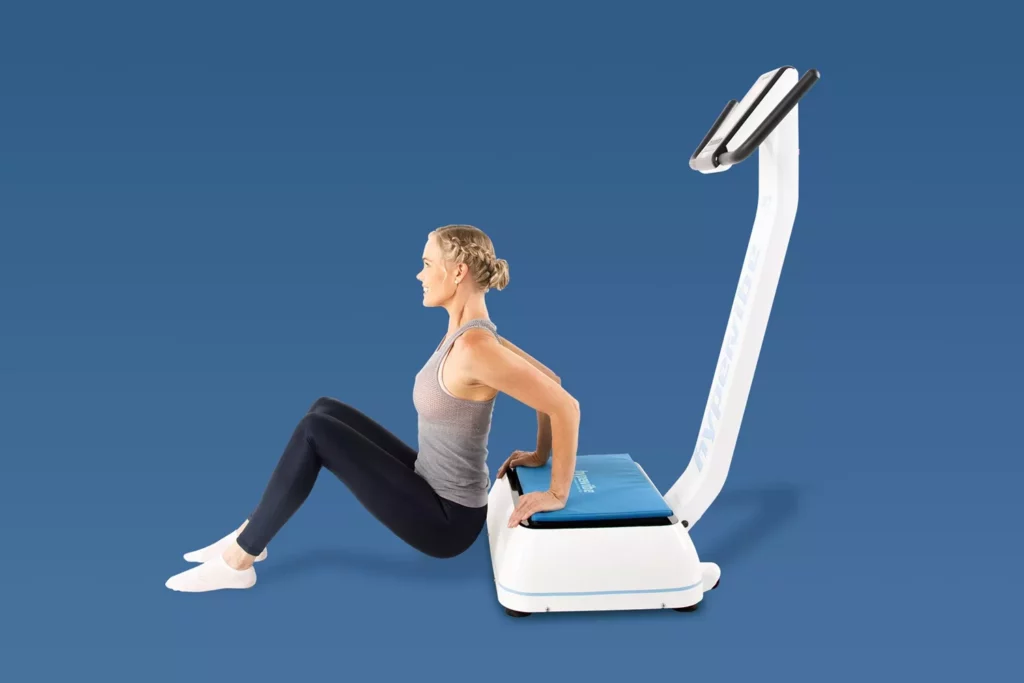 Top Vibration Plate Exercises: A Complete Guide To Safe Whole-Body Vibration Workouts 12 Woman performing tricep dips with her hands on a cushioned vibration plate and feet on the floor.