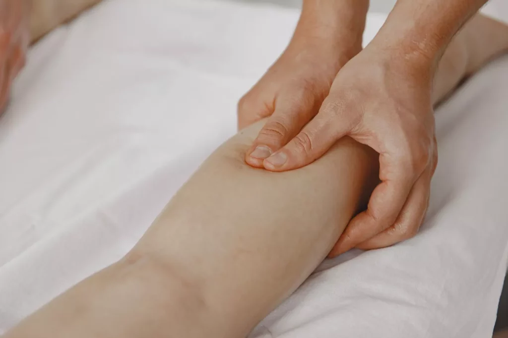 manual lymphatic drainage leg massage Close-up photograph of a therapist performing a manual lymphatic drainage massage technique on a client's calf muscle.