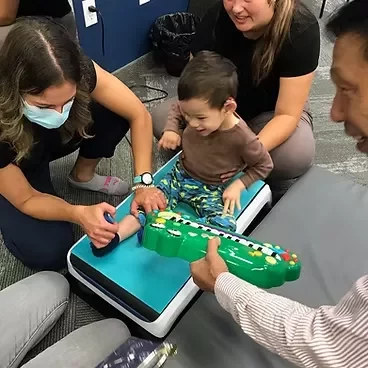 seated pediatric vibration plate exercise Toddler sitting on a blue pediatric vibration therapy platform playing with a toy keyboard during a rehabilitation session