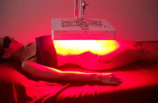 A woman lying on a bed receiving red light therapy from a specialized device placed over her abdomen
