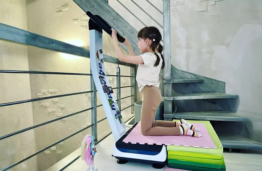 Child kneeling on a vibration plate with a pink mat on it